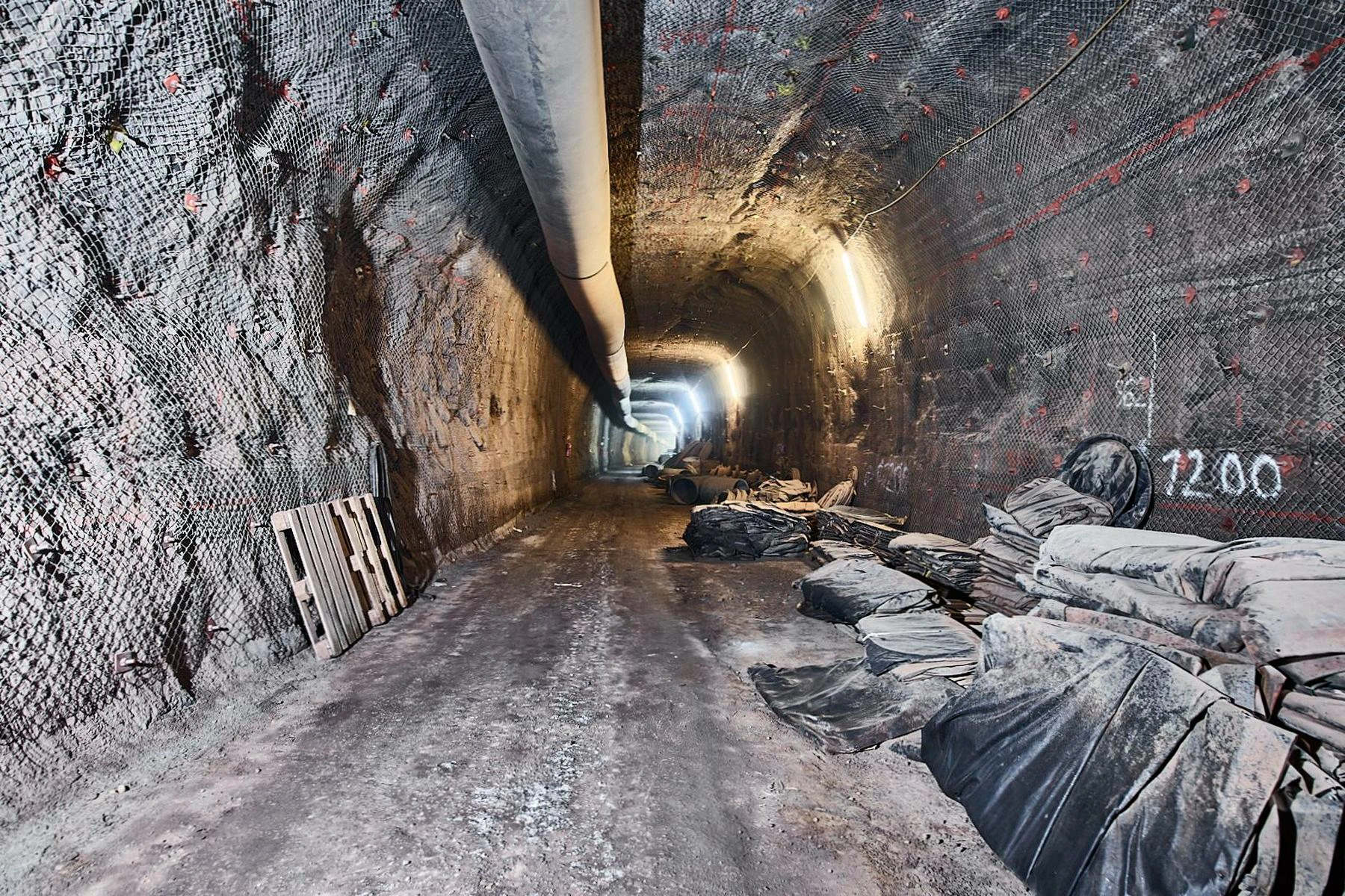 Ein unterirdischer langer Tunnel, an dessen Decke ein großes Rohr verläuft.