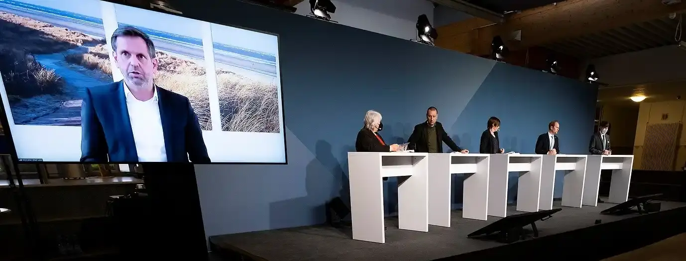 Vier Personen stehen an Pulten auf einem Podium.