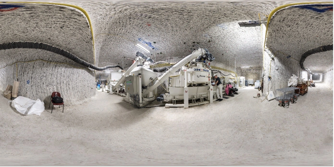 Panoramaaufnahme einer Baustoffanlage die in einer Strecke Salzbergwerks steht. An der rechten Seite steht ein Mann in Bergwerkskluft.