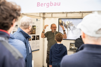 Ein BGE-Mitarbeiter aus dem Bereich Bergbau steht in einem Zelt. Besucher*innen hören ihm zu. Er erklärt seine Arbeit.