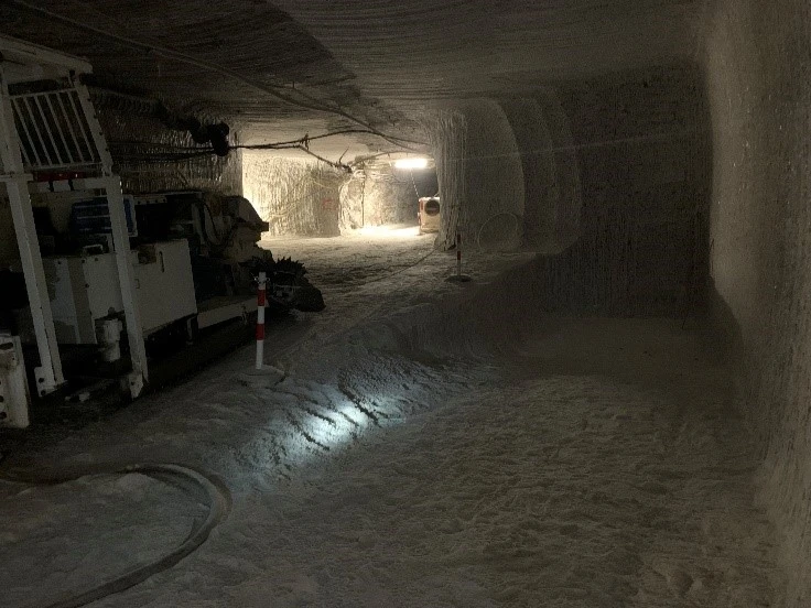 Unter Tage steht am Rand einer hell beleuchteten Strecke eine Teilschnittmaschine. Rechts davon ist eine kleine Schräge im Salzgestein erkennbar.