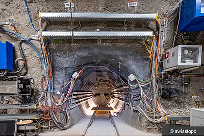Das Foto zeigt den Tunnel des FE-Experimentes im Felslabor Mont Terri, Schweiz. Der Tunnel ist mit zahlreichen Messgeräten und Sensoren ausgestattet. Aus dem Inneren des Tunnels verlaufen viele Kabelstränge zu Aufzeichnungsgeräten.
