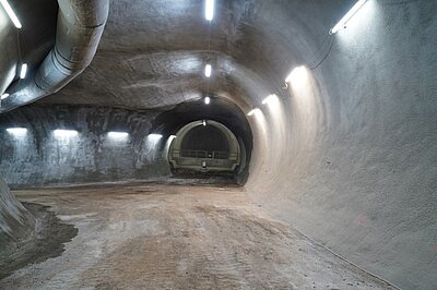 Wendestelle mit einer Fahrbahn aus verdichtetem Gesteinsschutt (Haufwerk), halbrunden, glatten, grauen Betonwänden und ebensolcher Firste. An die Wendestelle schließt sich im Hintergrund das Betonbauwerk des Waschplatzes an.