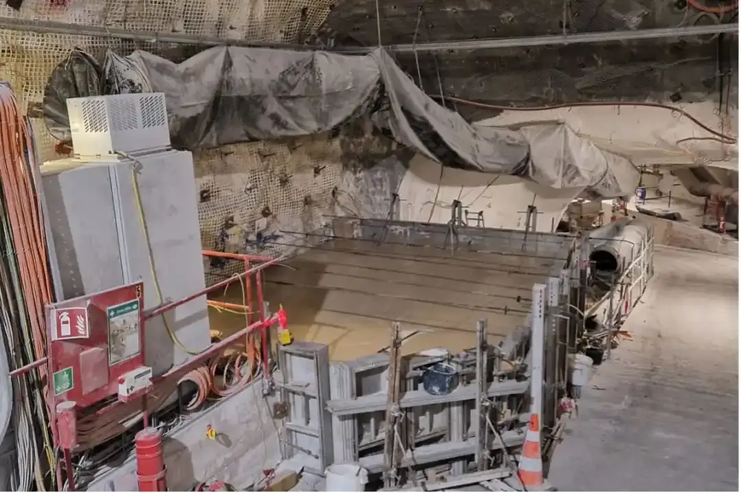 Das Bild zeigt den Blick in eine leicht abfallende Strecke in einem Bergwerk. Die Bildmitte zeigt einen mit Stahlwänden begrenzten Bereich, der mit flüssigem Beton verfüllt ist. Links im Vordergrund grenzen Elektroanlagen an diesen Bereich. Auf der rechten Seite führt ein abschüssiger Streckenteil an der Verschalung vorbei.  