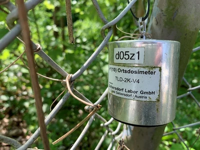 Das Bild zeigt ein Ortsdosimeter, das in unmittelbarer Nähe zur Schachtanlage Asse II angebracht ist. Das Ortsdosimeter ist silbern, zylindrisch und faustgroß.