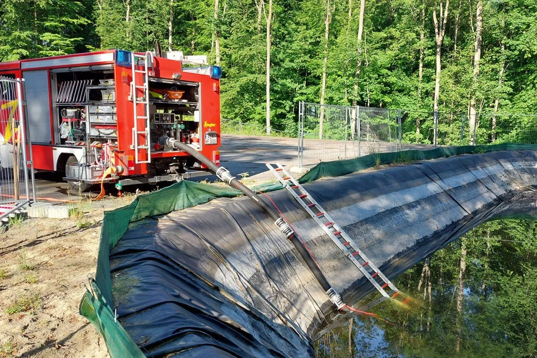 Aus einem Fahrzeug der Feuerwehr ragt ein Schlauch mit Pumpe in ein großes Becken, das mit Wasser gefüllt ist. 