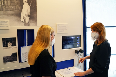 Zwei Frauen stehen vor einem kleinen Bildschirm in einem Ausstellungsraum