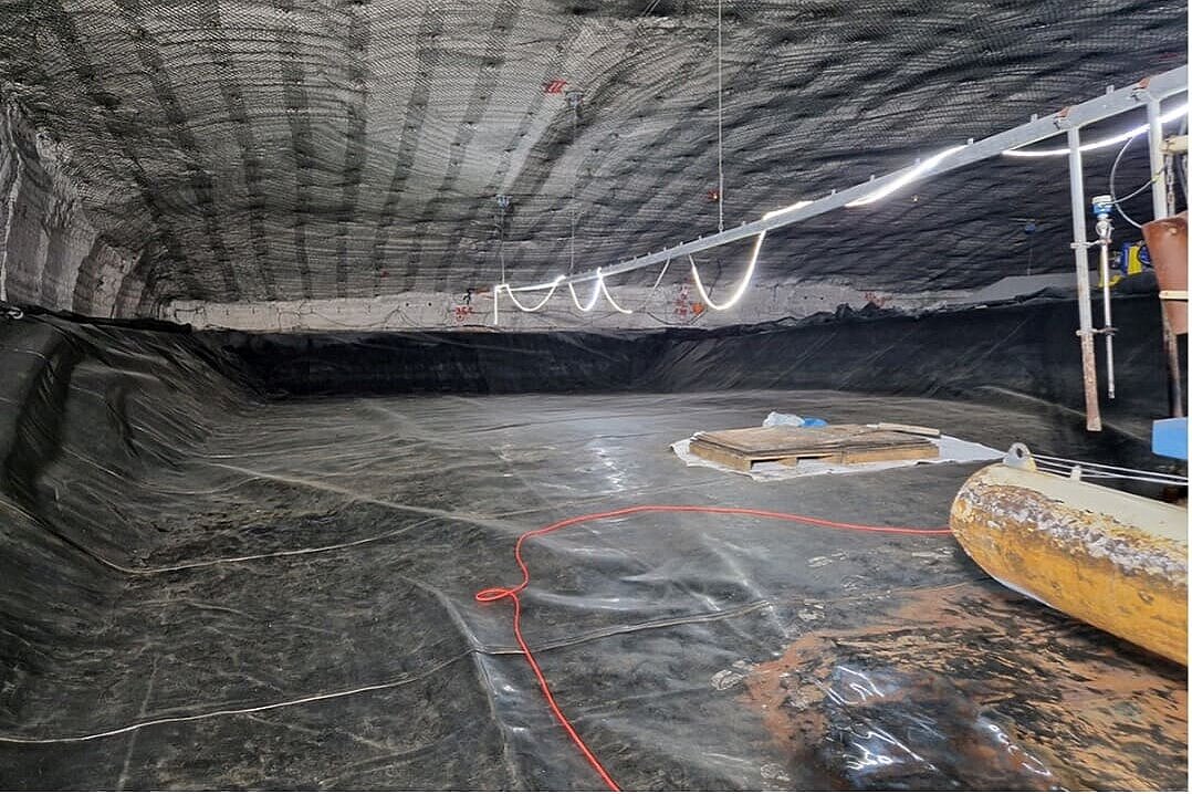 Das Bild zeigt den Blick in einen Salzabbau im Bergwerk. Die Decke des Abbaus wird von einer zaunartigen Struktur gesichert. Im Boden ist eine Art Becken ausgehoben in dem eine schwarze Folie verlegt ist. Im Vordergrund ist ein gelber Schwimmponton zu erkennen, der auf der Folie steht.