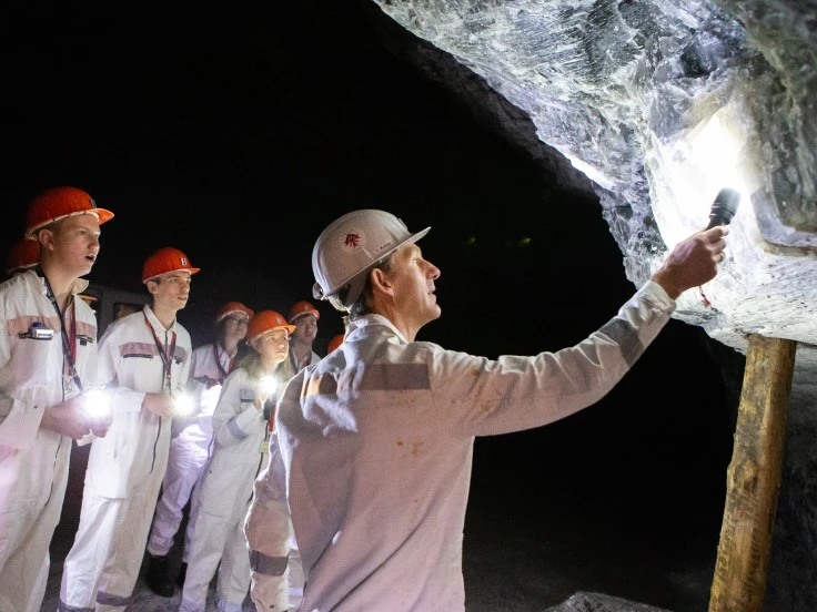 Das Bild zeigt eine Gruppe von Personen in Bergmannskleidung. Ein Mann leuchtet mit einer Taschenlampe das Gestein an.