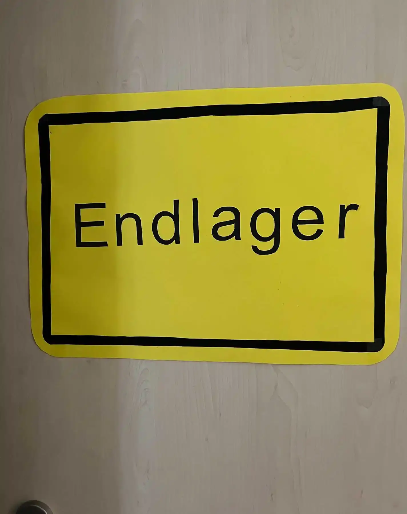 Ein Schild, das anmutet wie ein gelbes Ortsschild. Darauf steht "Endlager".