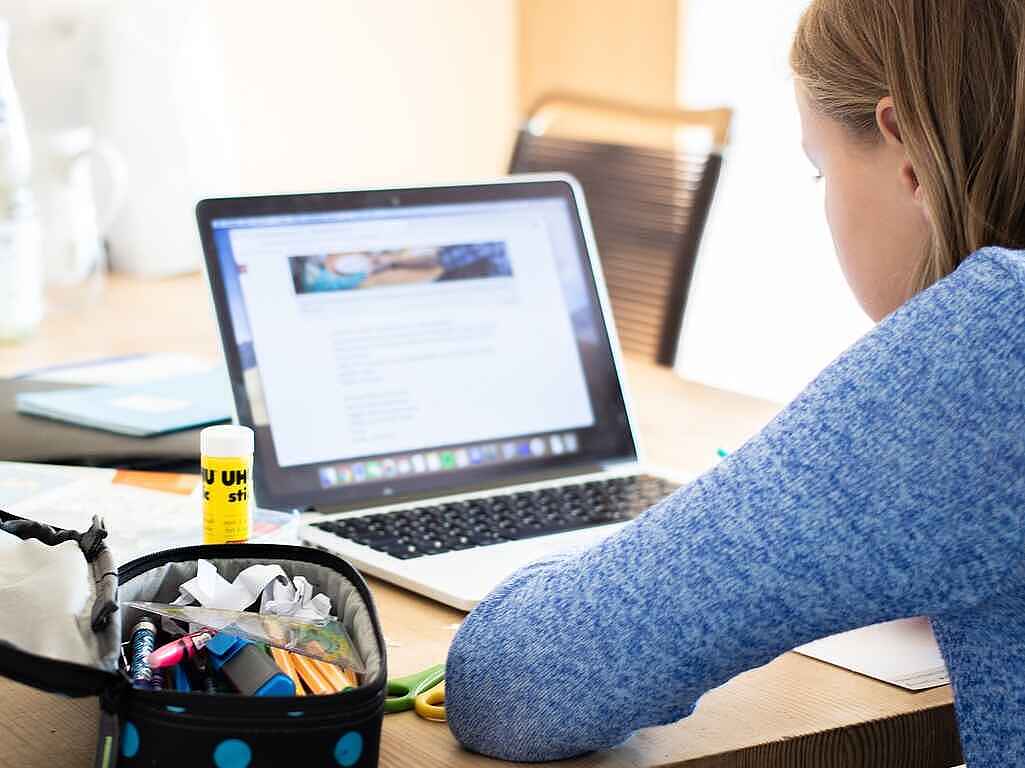 Ein Mädchen sitzt an einem Tisch vor einem aufgeklappten Laptop. Daneben liegt ein aufgeklapptes Etui.