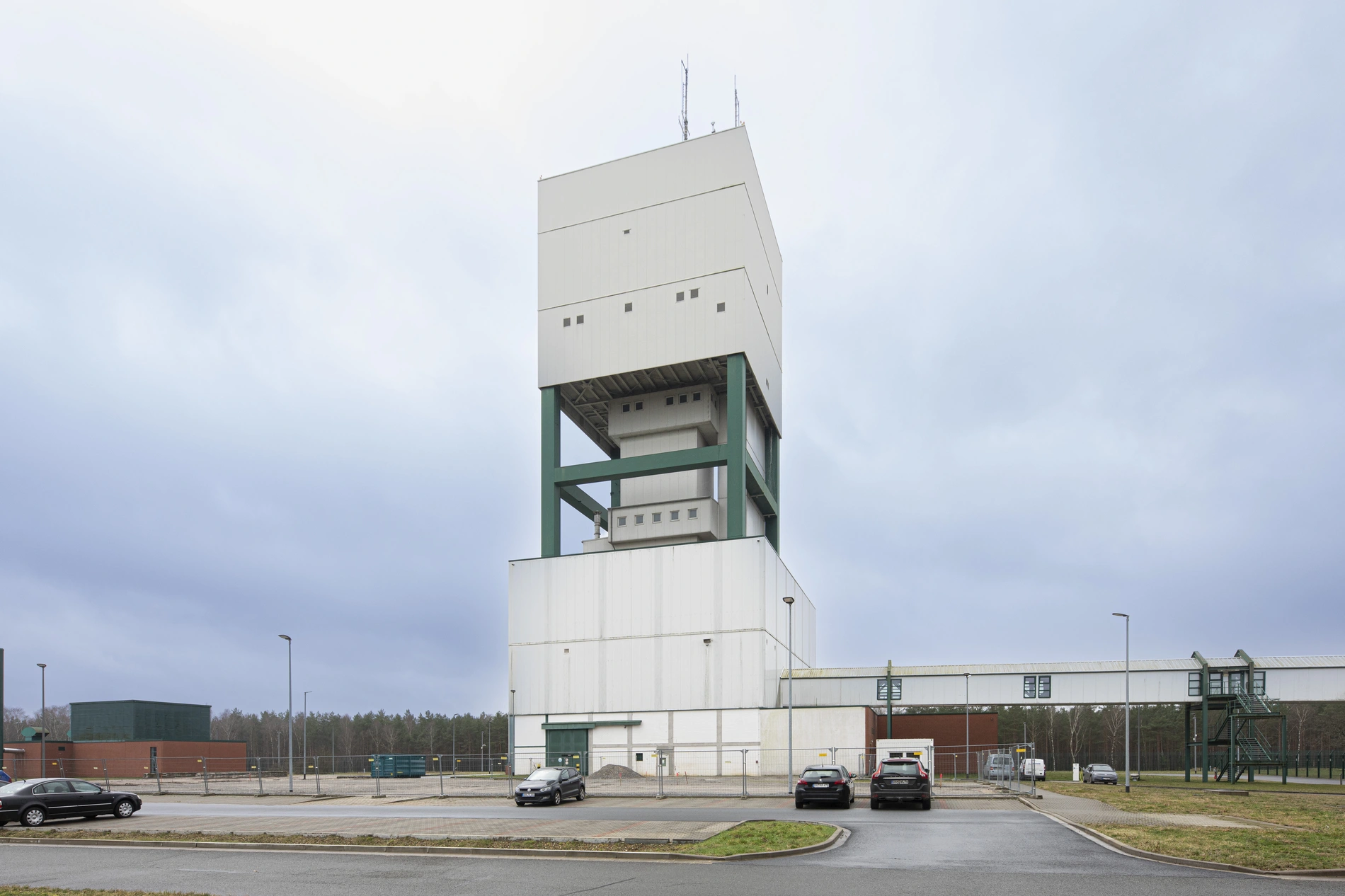 Der Förderturm des Bergwerks Gorleben - fotografiert vom davor liegenden Parkplatz aus, auf dem wenige Autos parken.