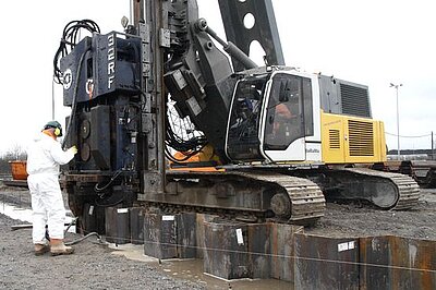 Ein Bagger rammt Spuntwände in die Erde