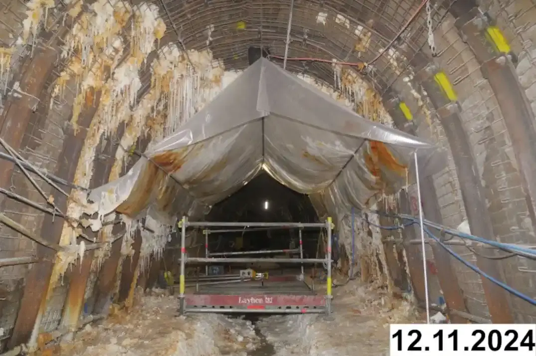 Foto einer bogenförmigen Strecke unter Tage. An den Seiten und der Decke bilden sich weiße Verkrustungen. Eine Plastikplane ist unter der Decke aufgespannt.