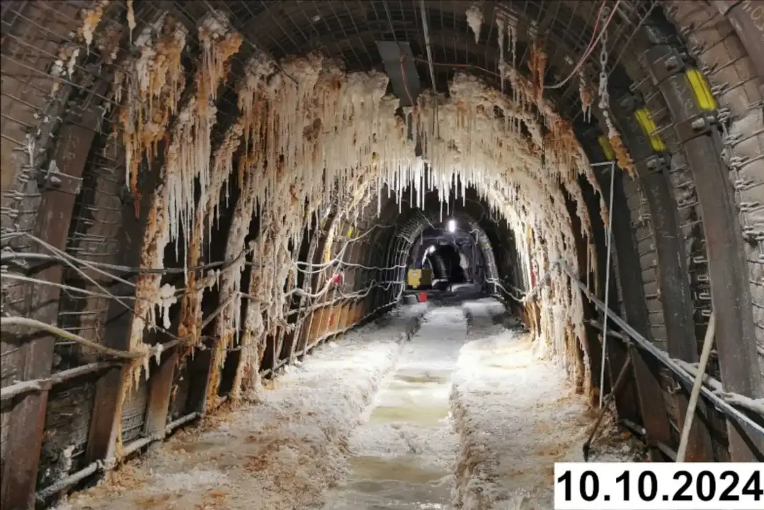 Foto einer bogenförmigen Strecke unter Tage. An den Seiten und der Decke bilden sich weiße Verkrustungen.