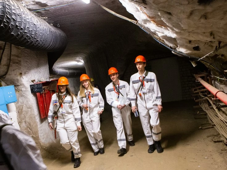 Das Bild zeigt vier Personen in Bergmannskleidung unter Tage in einer gehenden Bewegung