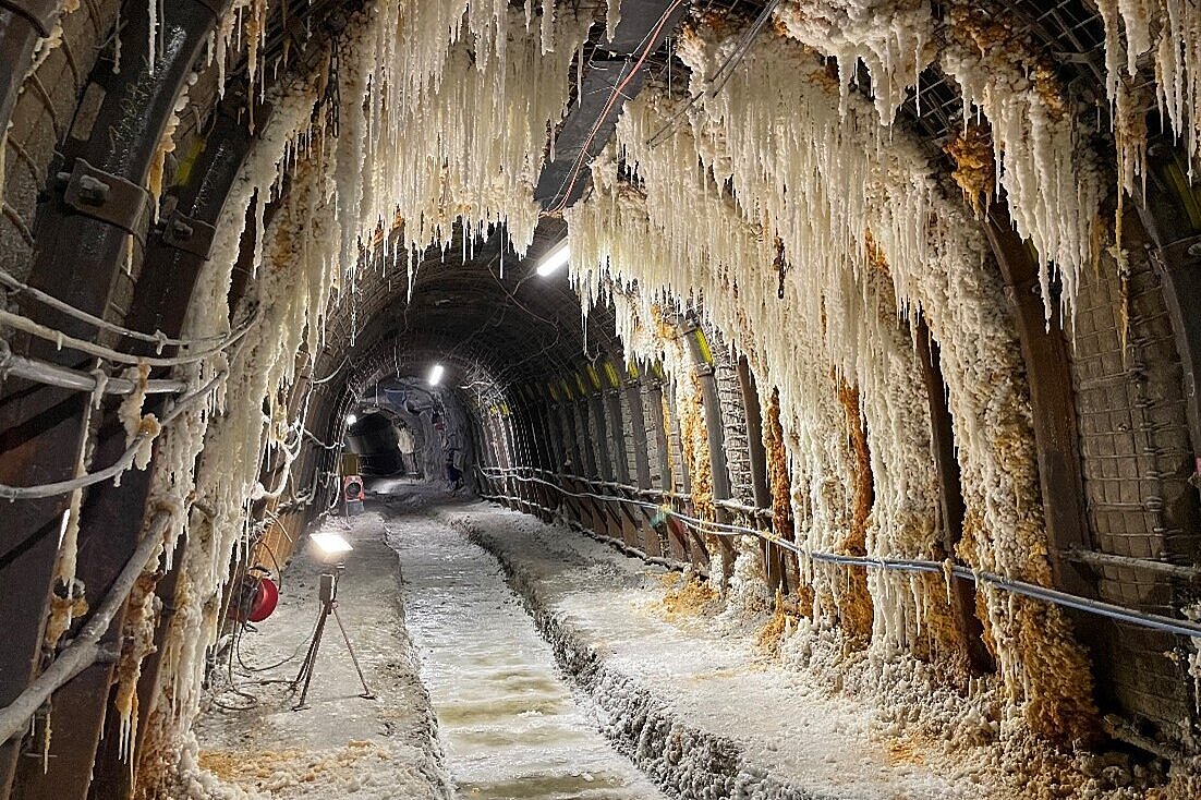 Das Bild zeigt eine Strecke unter Tage. Von der Decke hängen Salzzapfen. Im Boden verläuft ein Kanal, in dem sich Pfützen befinden.