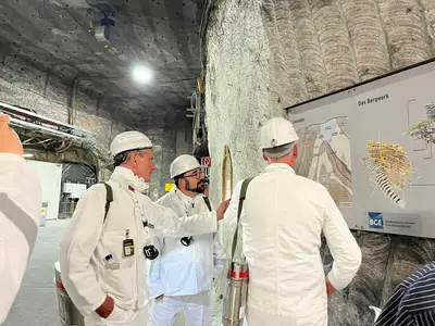 Drei Männer in weißer Bergmannskluft unterhalten sich unter Tage vor einer Schautafel. 