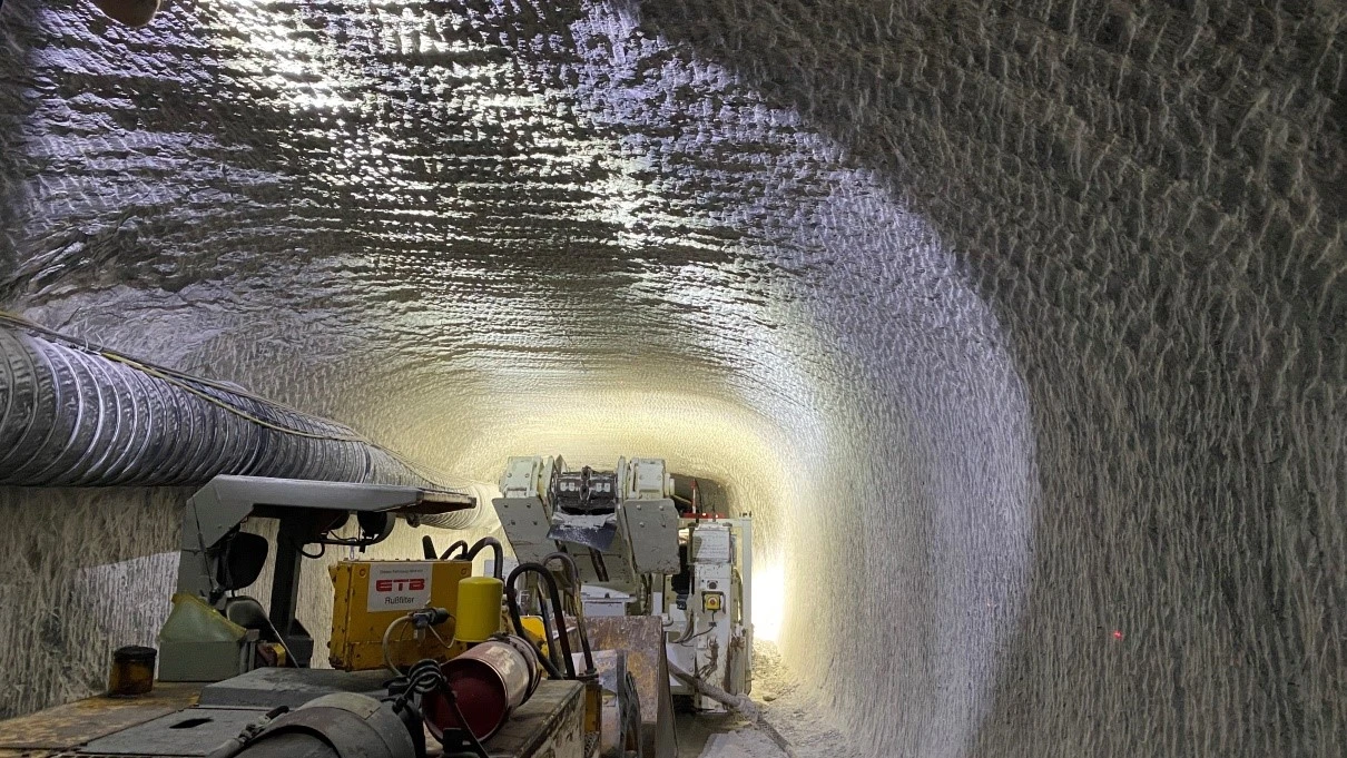 Eine große Maschine auf einem Kettenfahrwerk steht in einem Streckenabschnitt im Bergwerk Morsleben und fräst mit ihrem Schneidkopf Gestein aus der Kontur