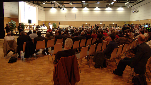 Publikum hört einem Vortrag zu. Zur Seite "Die Entscheidung zur Rückholung"