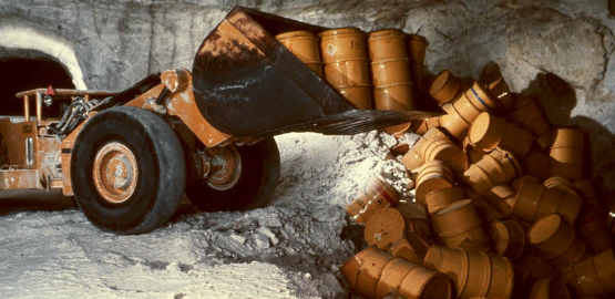 Underground: an excavator tips barrels onto a pile. Link to page "Radioactive waste in the Asse II mine"
